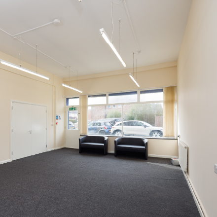 Spacious community room with large front windows, seating, and flexible space for meetings and activities.