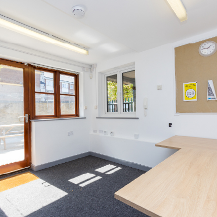 Small meeting room with desk space, noticeboard, and access to an outdoor area through a glass door.