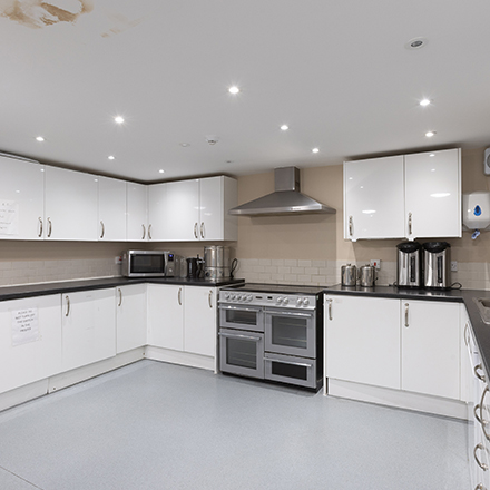 Modern communal kitchen with white cupboards, worktops, cooking appliances, and tea and coffee facilities.