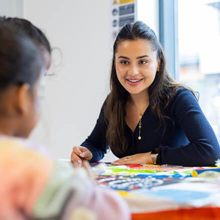 Young girl focuses on colouring while another child works beside her at a craft table.
