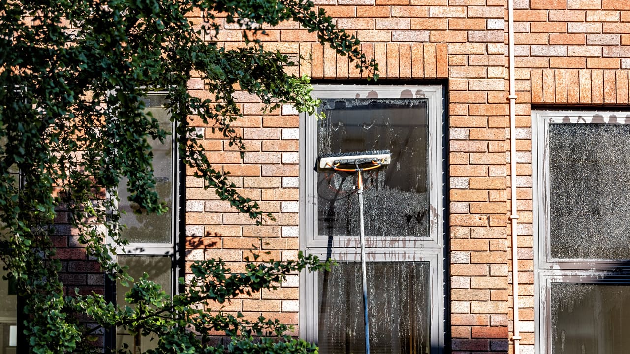 Window cleaning in progress on a brick building, with water streaming down the glass under a sunny sky